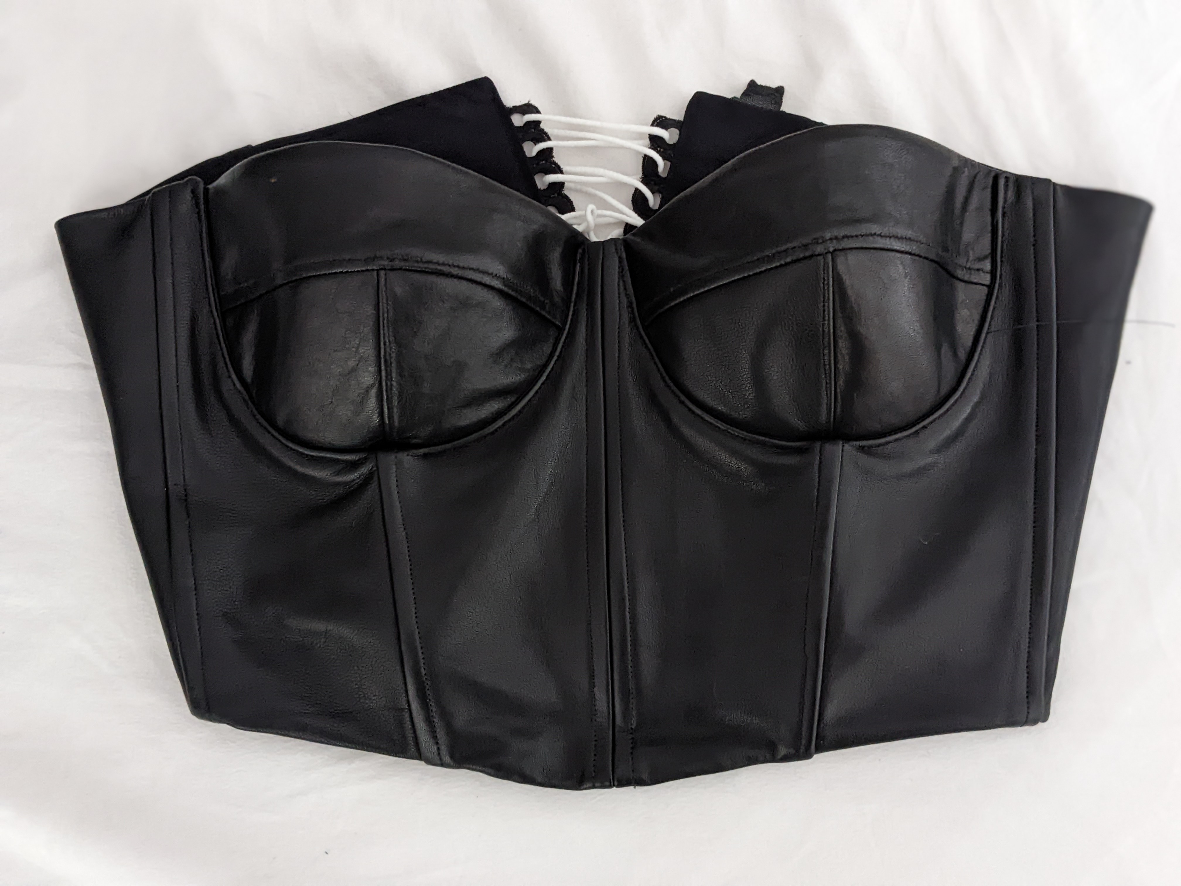 flat lay of a black leather bustier layed flat on a white bedsheet