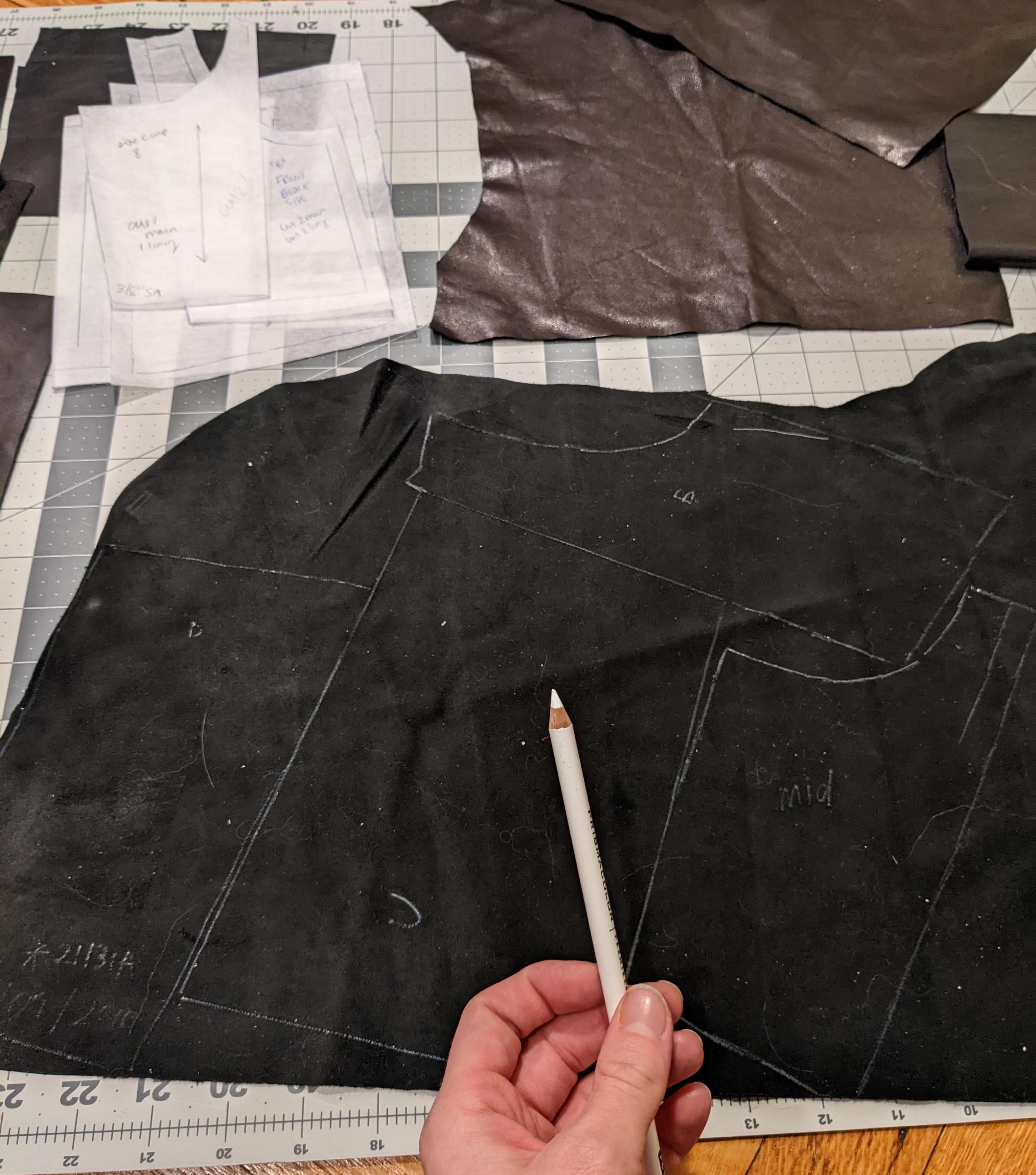 Gracie's hand holding a white pencil over a piece of black leather with pattern pieces marked