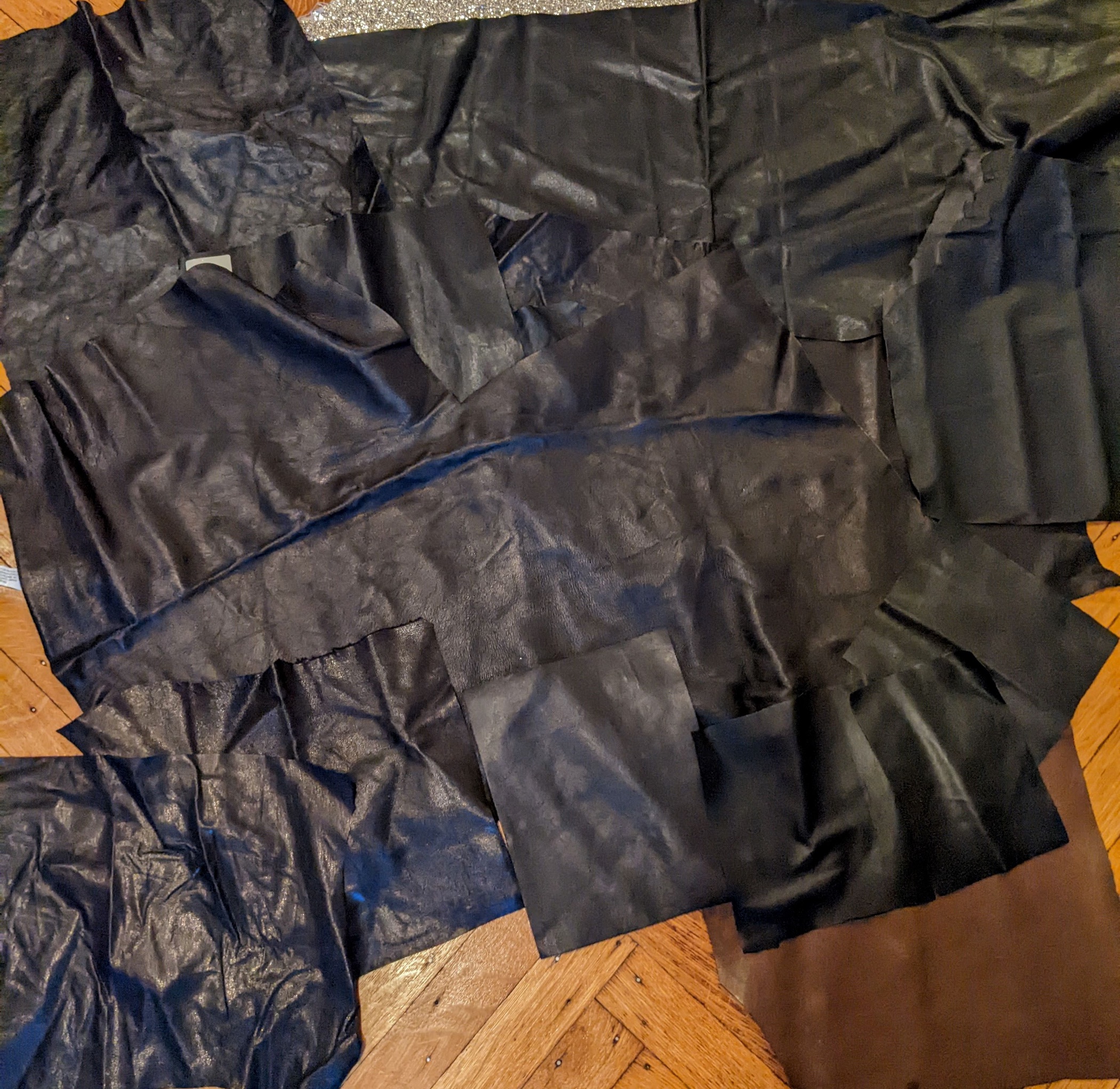 Photo of black leather scraps layed next to each other on a wooden floor.